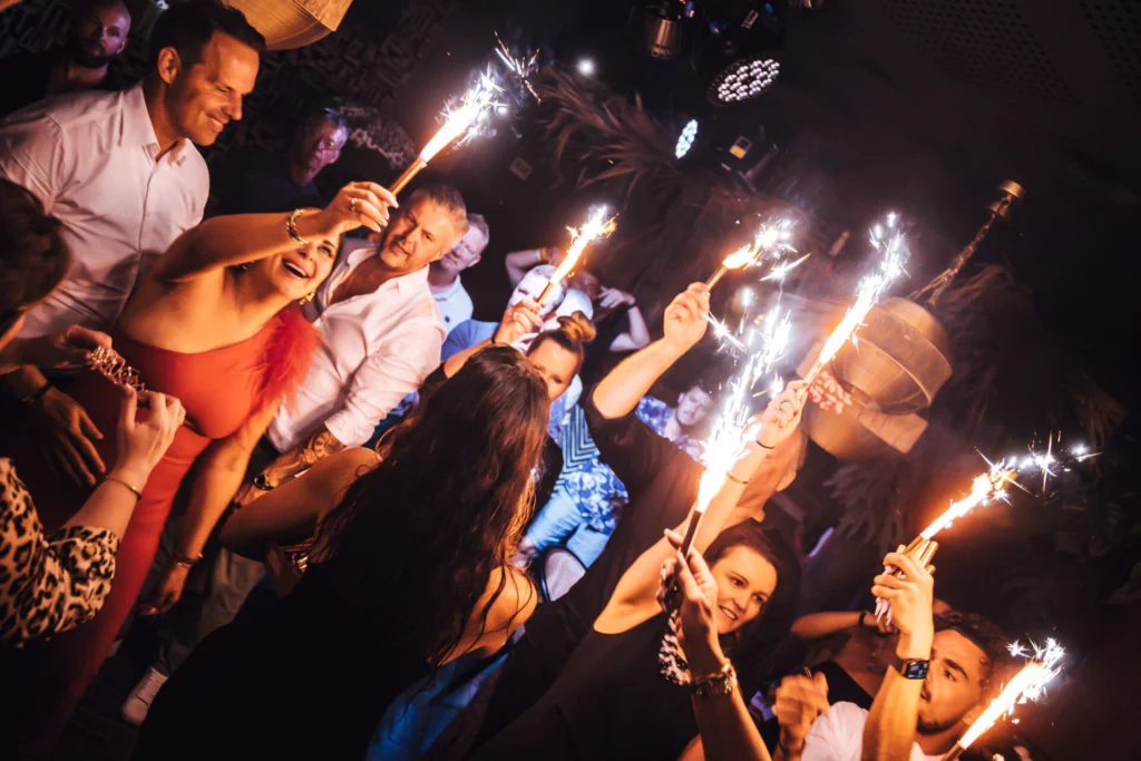 Foto scattata di sera nella sala spettacoli "festosa" del Monkey Ibiza. Si vedono persone che tengono in mano delle stelline luminose e sorridono.